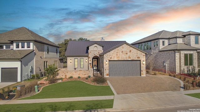 french provincial home featuring metal roof, driveway, stone siding, an attached garage, and a standing seam roof