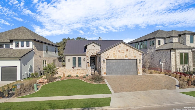 french country inspired facade with a front lawn, a chimney, decorative driveway, stone siding, and an attached garage