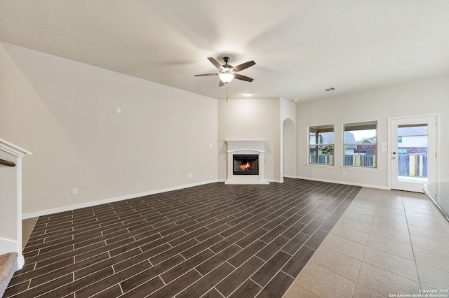 unfurnished living room featuring ceiling fan, a lit fireplace, dark wood-style floors, and baseboards