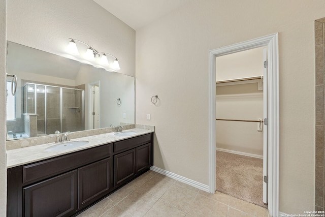 full bath with double vanity, a stall shower, a walk in closet, and a sink