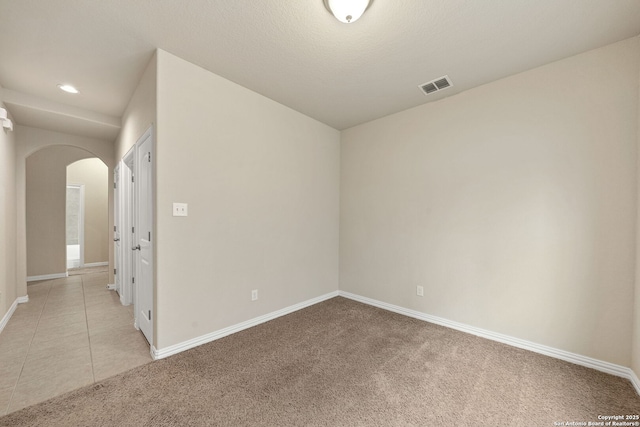 spare room with light carpet, light tile patterned floors, baseboards, visible vents, and arched walkways