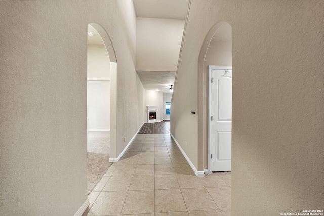 corridor with light tile patterned floors, baseboards, arched walkways, and a textured wall