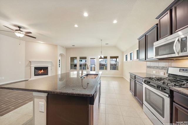 kitchen featuring an island with sink, a sink, stainless steel appliances, dark brown cabinets, and backsplash