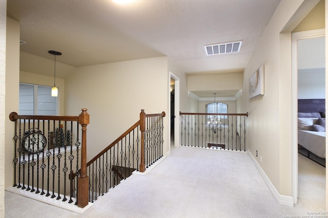 hallway with a chandelier, visible vents, an upstairs landing, baseboards, and carpet