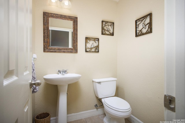 half bathroom with toilet, baseboards, a sink, and tile patterned floors