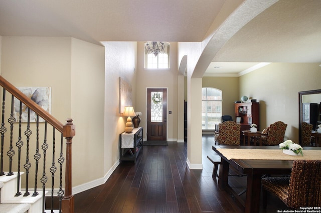 foyer with arched walkways, a notable chandelier, dark wood-type flooring, baseboards, and stairs