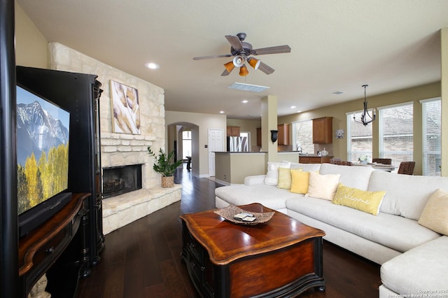 living area with visible vents, arched walkways, dark wood-style floors, ceiling fan, and a stone fireplace