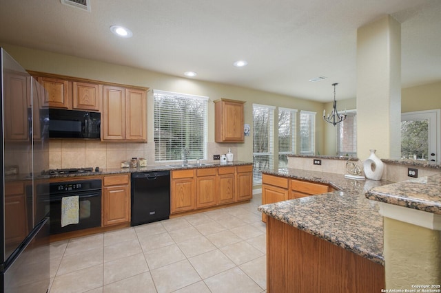 kitchen featuring a notable chandelier, a sink, backsplash, black appliances, and dark stone countertops