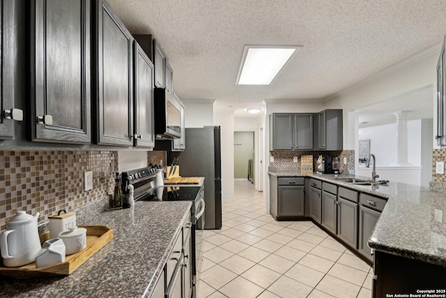 kitchen featuring light tile patterned floors, stainless steel appliances, a sink, tasteful backsplash, and dark stone countertops