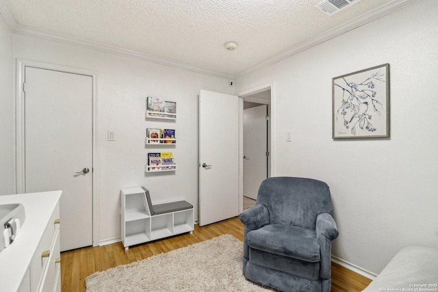 living area featuring a textured ceiling, ornamental molding, visible vents, and light wood-style floors