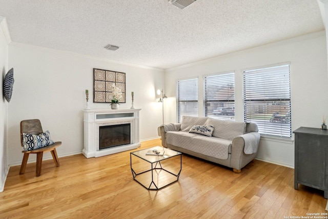 living room with a glass covered fireplace, crown molding, light wood-style flooring, and a textured ceiling