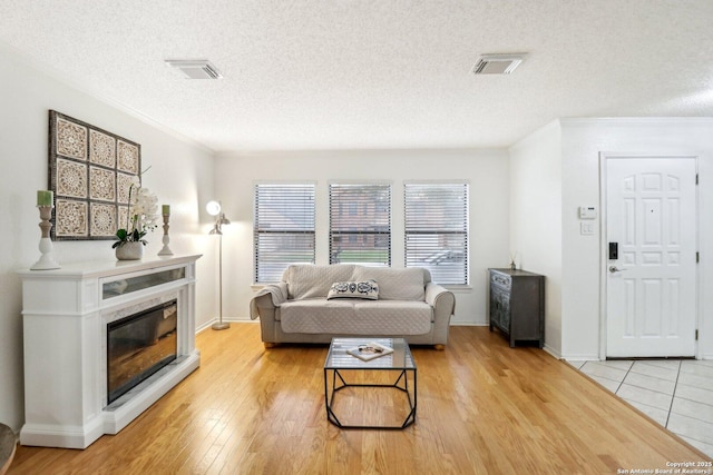 living area with light wood finished floors, a glass covered fireplace, visible vents, and crown molding