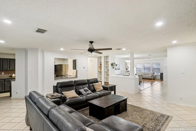 living area featuring a ceiling fan, light tile patterned flooring, a textured ceiling, and ornate columns