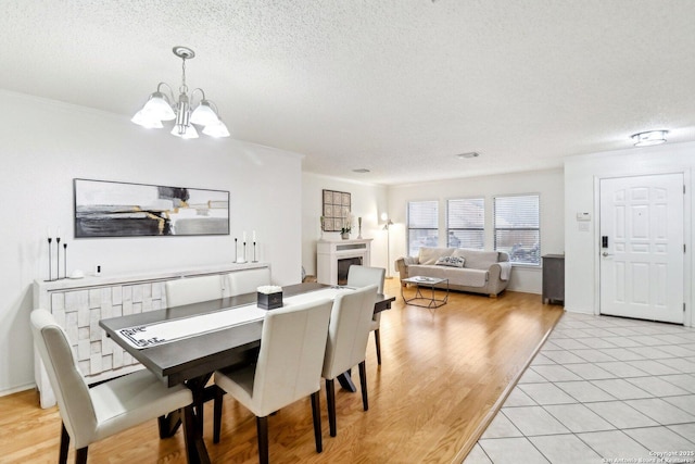 dining room featuring a textured ceiling, a fireplace, a chandelier, and light wood-style floors