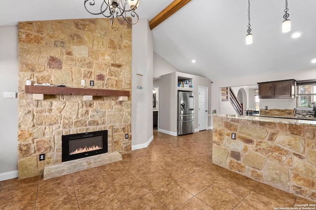 kitchen with a stone fireplace, dark brown cabinets, stainless steel refrigerator with ice dispenser, pendant lighting, and beamed ceiling