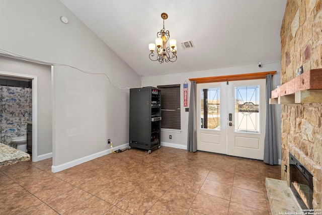 entrance foyer featuring visible vents, baseboards, vaulted ceiling, a stone fireplace, and an inviting chandelier