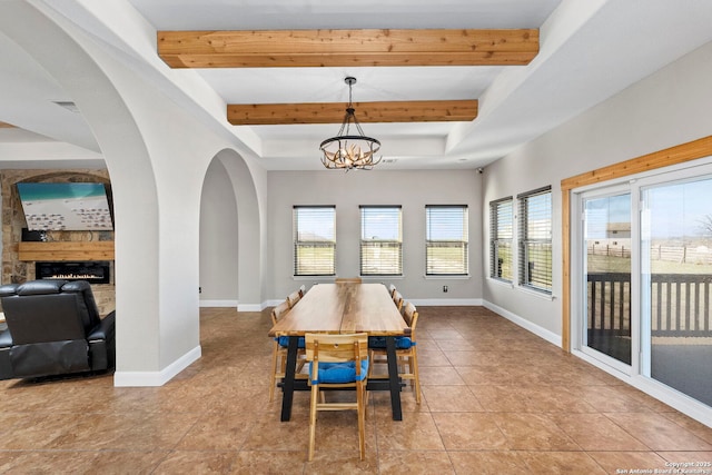 tiled dining room with beamed ceiling, baseboards, and a warm lit fireplace