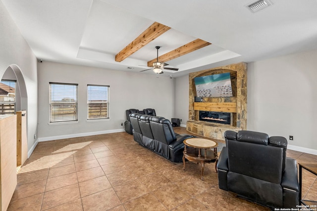 living room with baseboards, visible vents, a tray ceiling, a stone fireplace, and tile patterned flooring