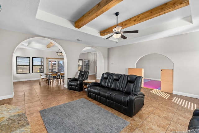 tiled living room featuring beamed ceiling, baseboards, a raised ceiling, and ceiling fan