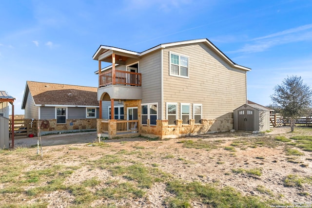 back of property with fence, a balcony, an outbuilding, stone siding, and a storage unit