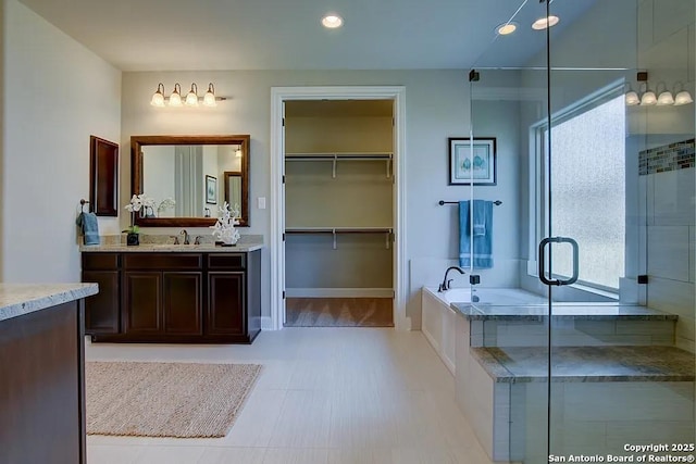 bathroom featuring a walk in closet, a garden tub, recessed lighting, vanity, and a shower stall