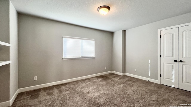 unfurnished bedroom featuring a textured ceiling, baseboards, dark colored carpet, and a closet