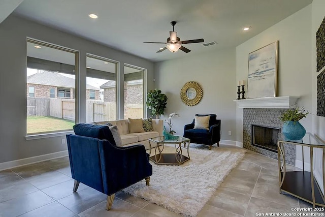 living room featuring ceiling fan, tile patterned flooring, a tile fireplace, visible vents, and baseboards