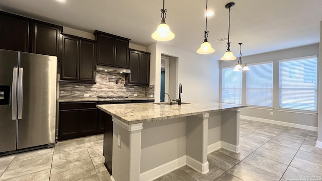 kitchen with under cabinet range hood, appliances with stainless steel finishes, backsplash, a center island with sink, and decorative light fixtures