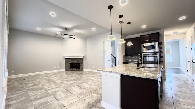 kitchen featuring visible vents, light stone counters, stainless steel appliances, a brick fireplace, and a sink