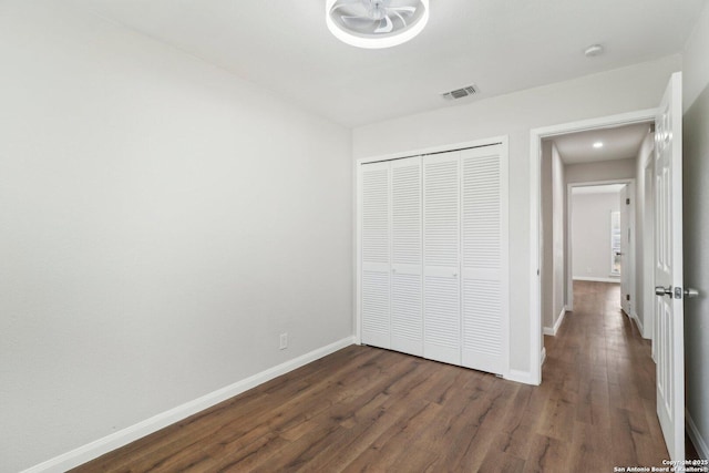 unfurnished bedroom with a closet, visible vents, dark wood finished floors, and baseboards