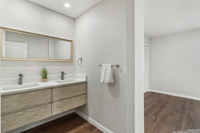 bathroom with double vanity, baseboards, a sink, and wood finished floors