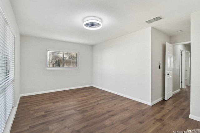 unfurnished room featuring dark wood-style floors, visible vents, and baseboards