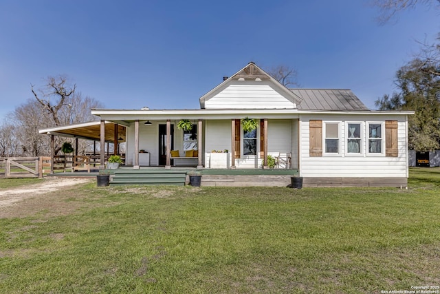 farmhouse with a front yard, covered porch, fence, and metal roof