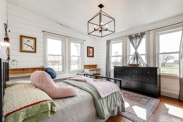 bedroom with a notable chandelier, vaulted ceiling, wooden walls, and wood finished floors