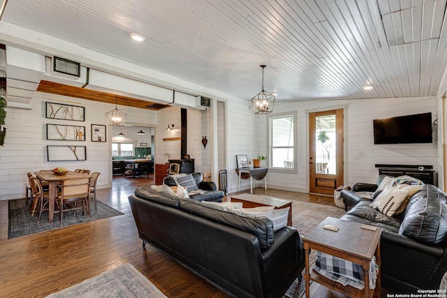 living area featuring a wood stove, a healthy amount of sunlight, a notable chandelier, and wood finished floors