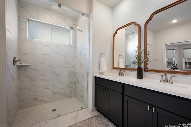 bathroom with double vanity, marble finish floor, tiled shower, and a sink