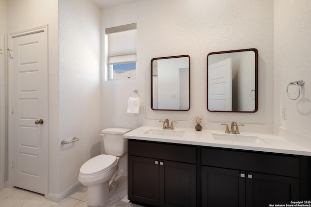 bathroom with double vanity, a sink, toilet, and baseboards