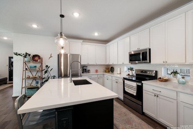 kitchen with a sink, light countertops, appliances with stainless steel finishes, decorative backsplash, and decorative light fixtures