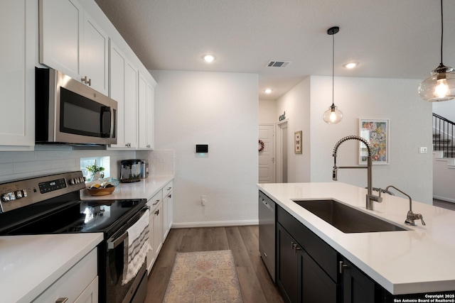 kitchen featuring tasteful backsplash, a center island with sink, dark wood finished floors, stainless steel appliances, and a sink