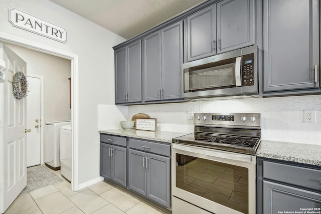 kitchen featuring tasteful backsplash, appliances with stainless steel finishes, gray cabinets, and washing machine and clothes dryer