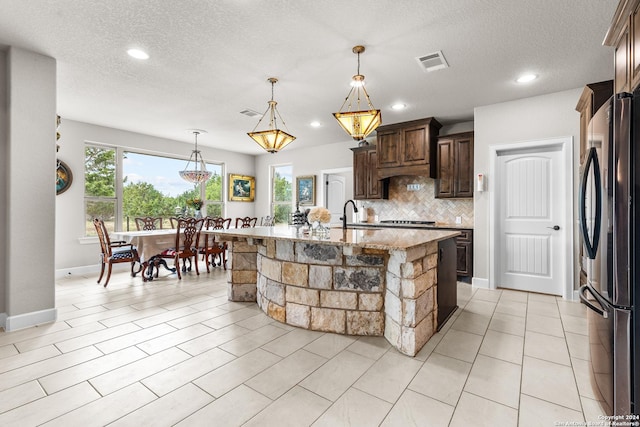 kitchen with light stone counters, stainless steel appliances, visible vents, decorative backsplash, and dark brown cabinets