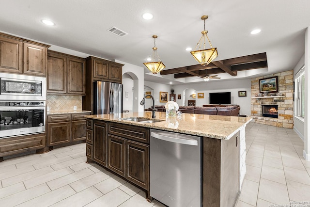 kitchen featuring arched walkways, a stone fireplace, a sink, visible vents, and appliances with stainless steel finishes