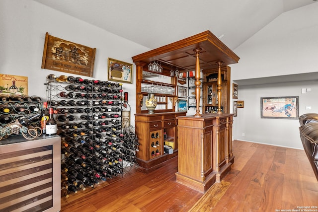 wine room with wine cooler, lofted ceiling, a bar, and wood finished floors