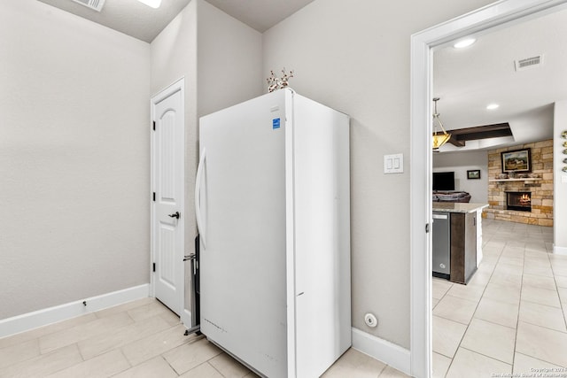 kitchen with a stone fireplace, visible vents, baseboards, stainless steel dishwasher, and freestanding refrigerator