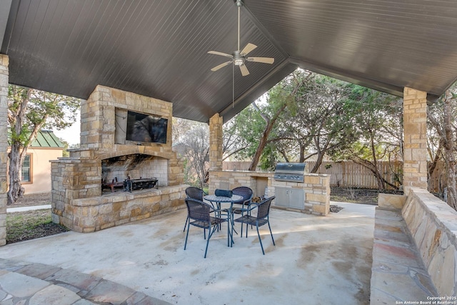 view of patio with ceiling fan, an outdoor stone fireplace, fence, exterior kitchen, and grilling area