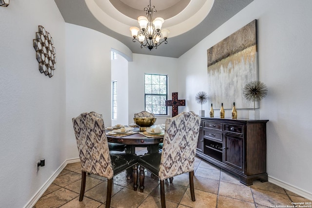 dining space featuring a chandelier, a raised ceiling, and baseboards