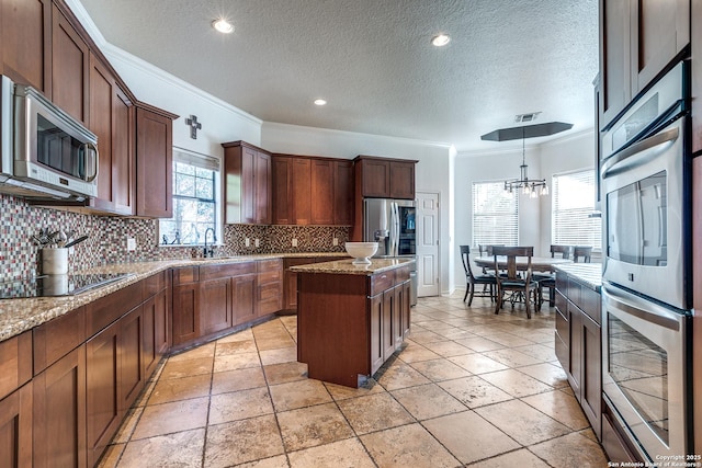 kitchen featuring decorative backsplash, ornamental molding, light stone countertops, stainless steel appliances, and a sink