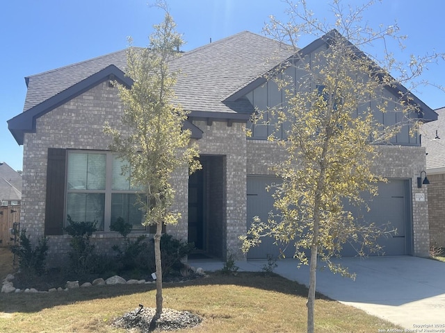 view of front of house with brick siding, roof with shingles, concrete driveway, a front yard, and a garage