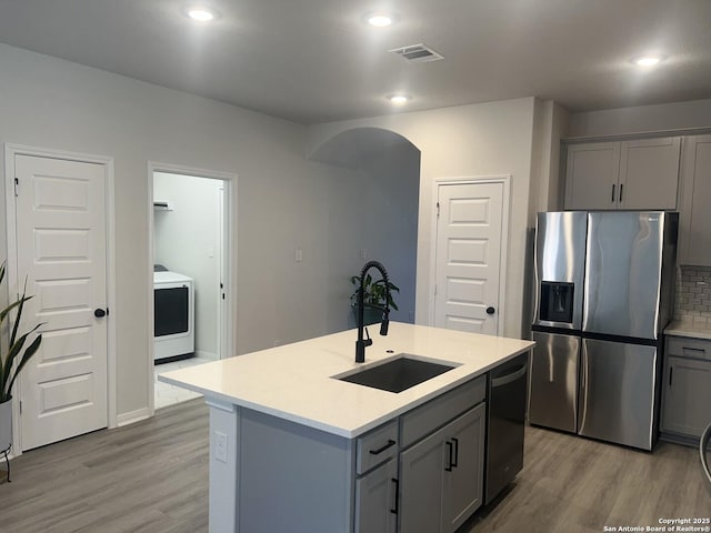 kitchen featuring stainless steel refrigerator with ice dispenser, gray cabinetry, a sink, washer / dryer, and dishwasher