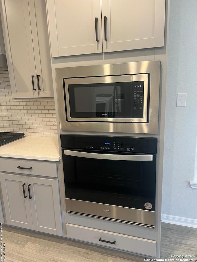 details with black gas cooktop, wall oven, light wood-style flooring, tasteful backsplash, and stainless steel microwave